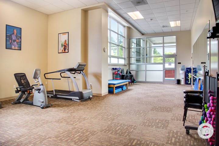 A spacious gym area with a treadmill and large windows letting in natural light.