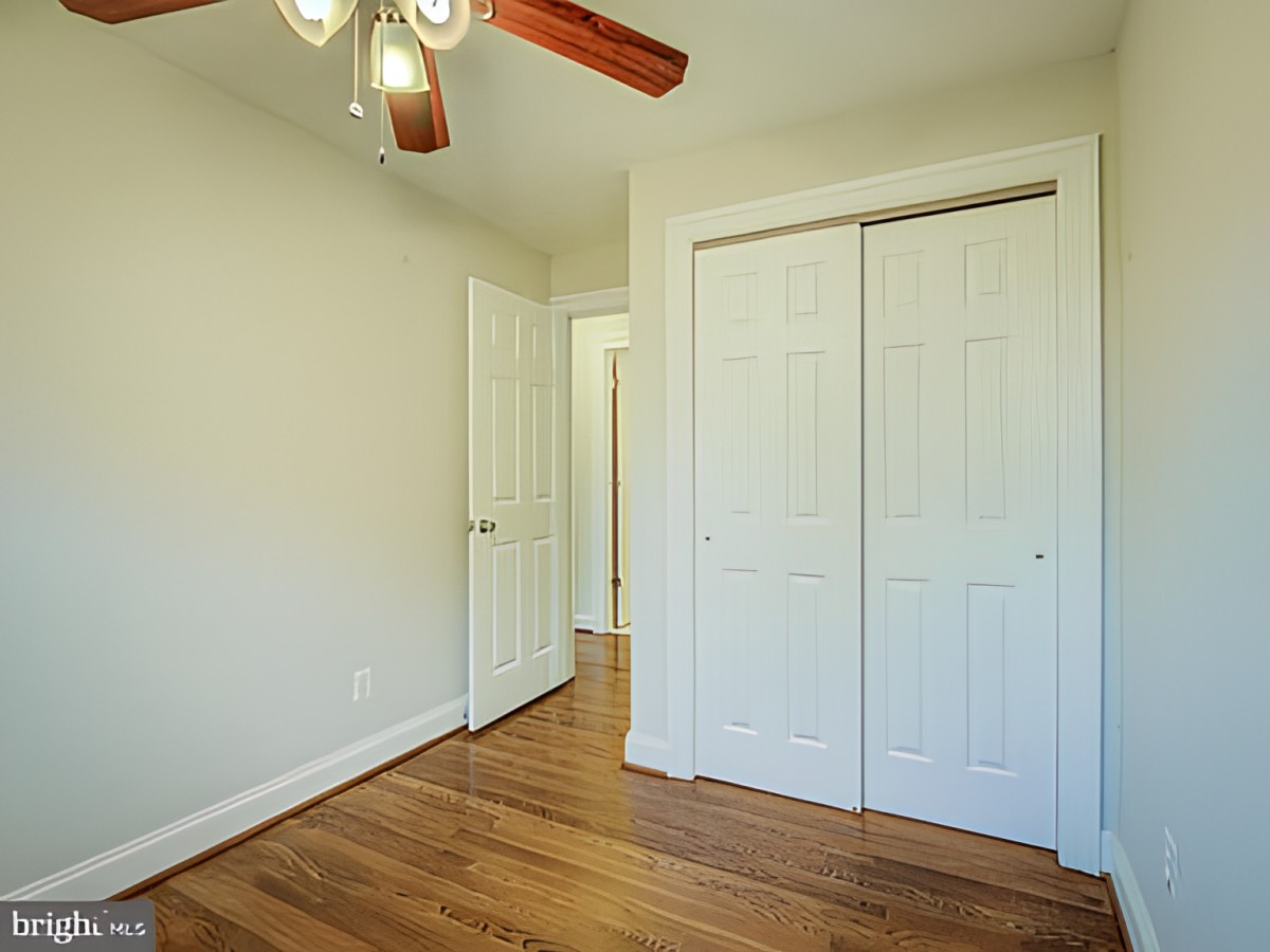 An empty room with wooden flooring, a ceiling fan, and a double-door closet.