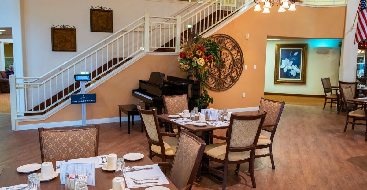A cozy dining area with elegant table settings, a piano, and a decorative staircase in the background.