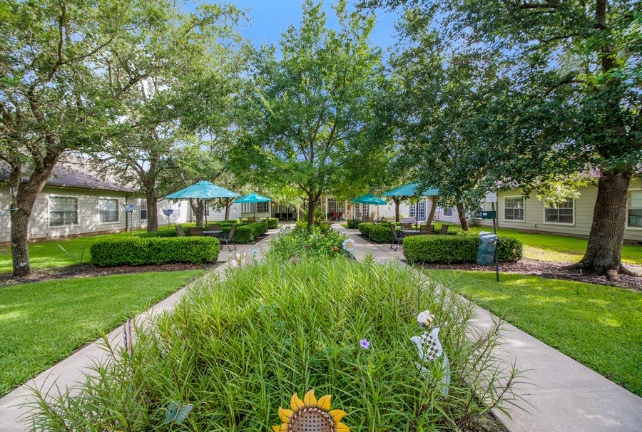 A beautifully landscaped garden with pathways, lush greenery, and outdoor seating areas under umbrellas.