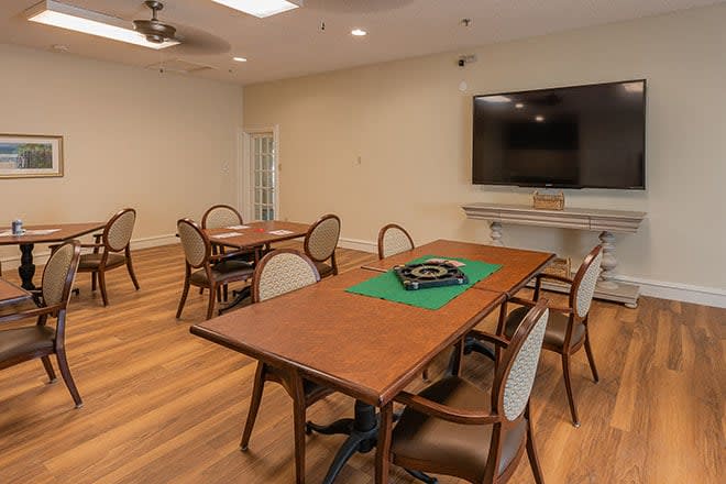 A well-lit meeting room with several tables and chairs, featuring a large television on the wall and a ceiling fan.