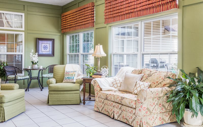 A cozy living room with patterned furniture, a lamp, and large windows.