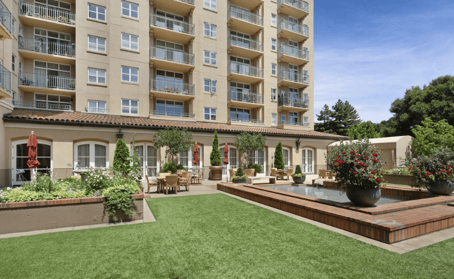 A view of a residential apartment building with a beautifully landscaped garden and outdoor seating area.