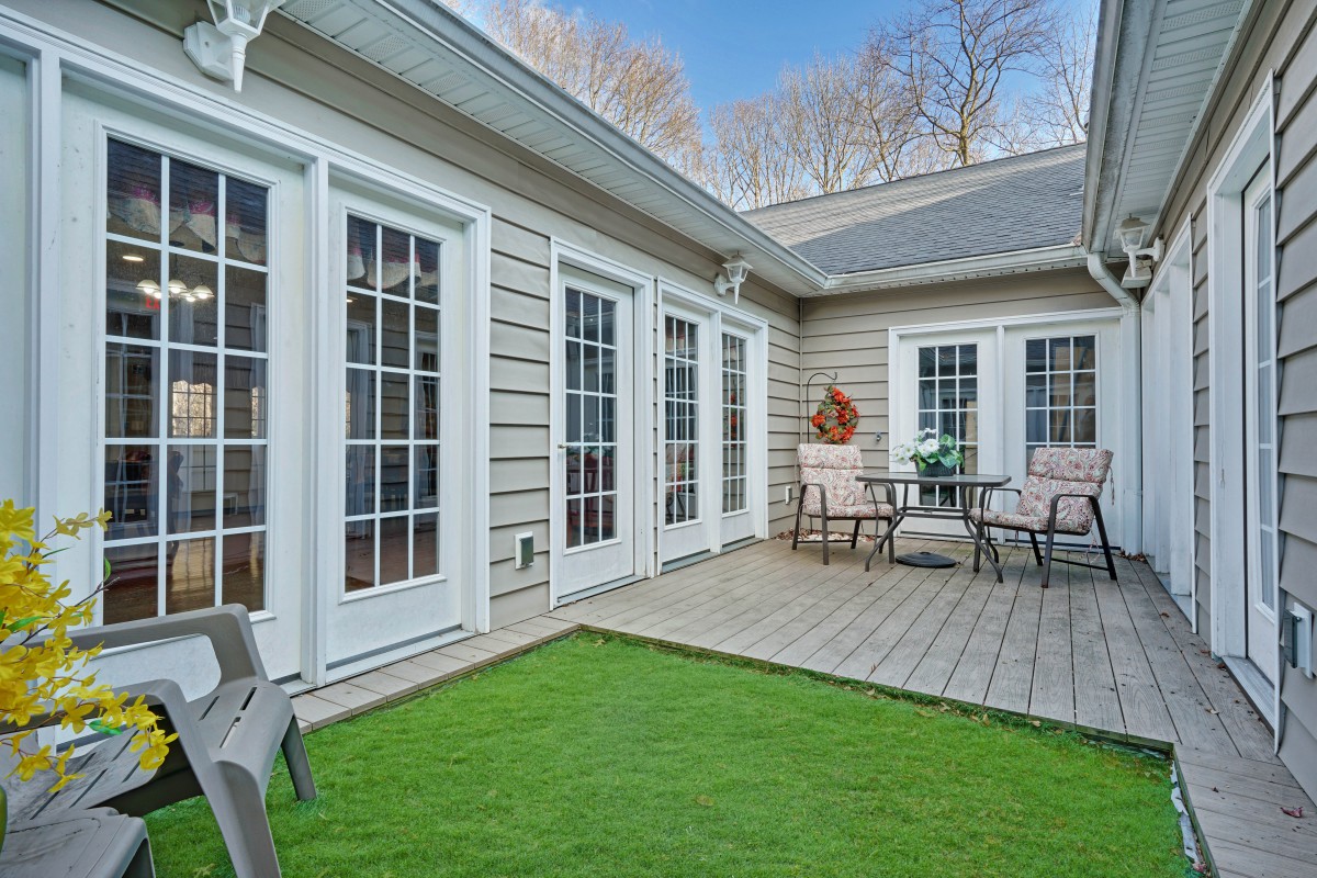 A cozy residential patio with artificial grass and outdoor seating, surrounded by elegant French doors.