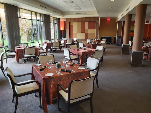 A spacious and elegantly arranged dining room with tables set for guests, featuring large windows that offer a view to the outdoors.