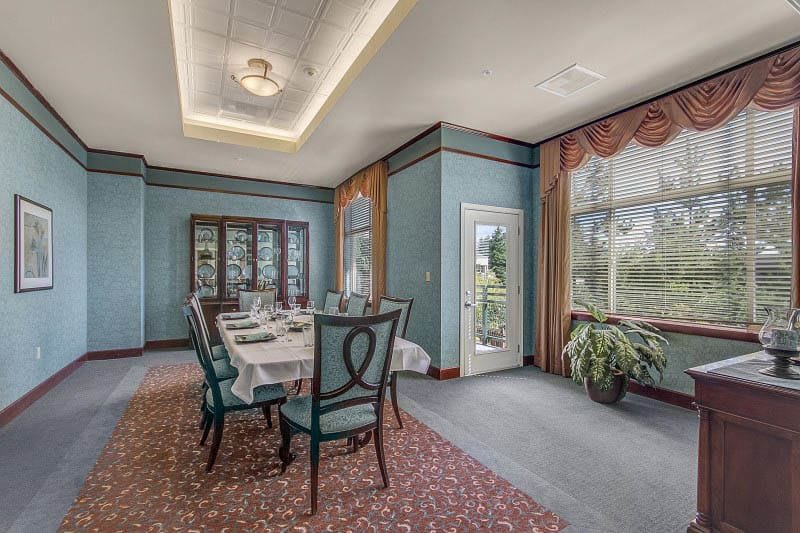 A formal dining room with a long table, elegant chairs, and large windows adorned with curtains.