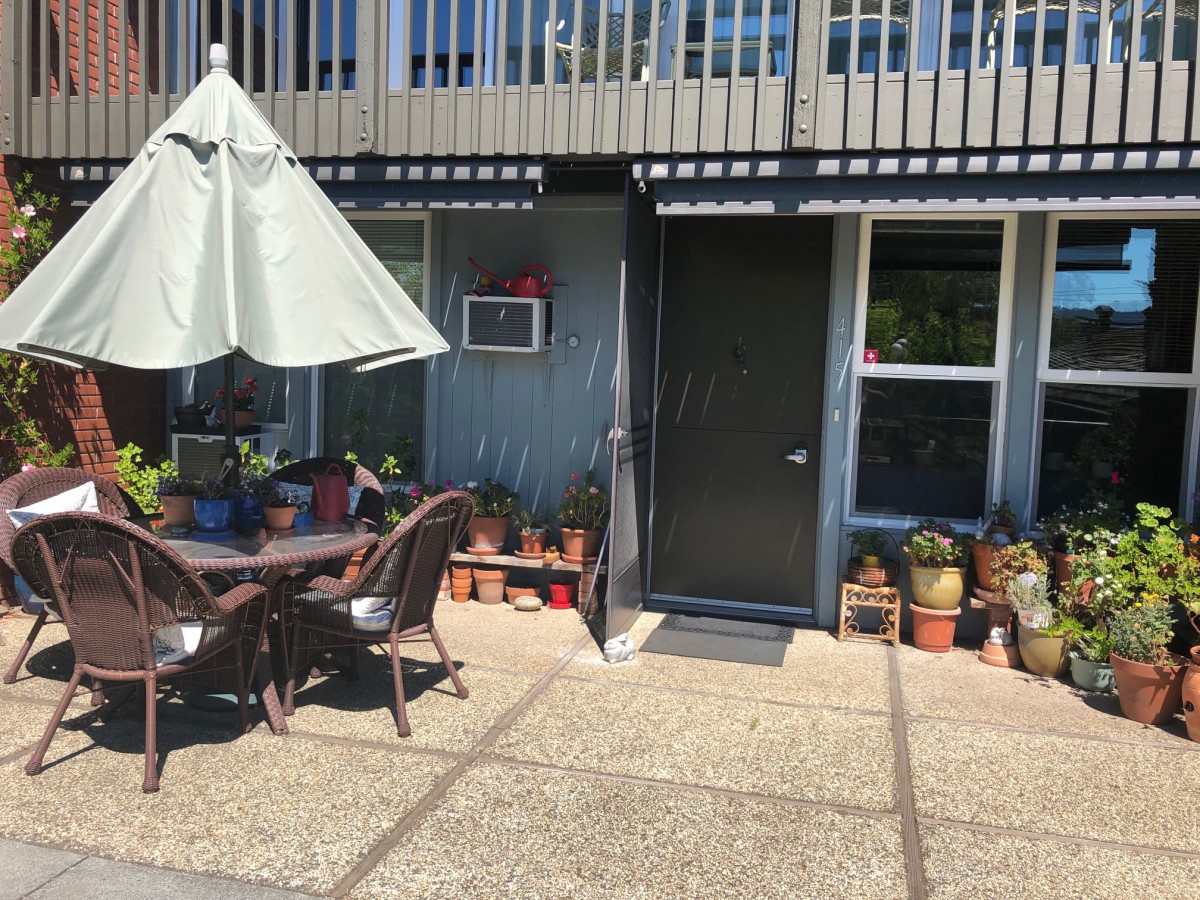 An inviting outdoor patio area with a sunshade, seating, and various potted plants.