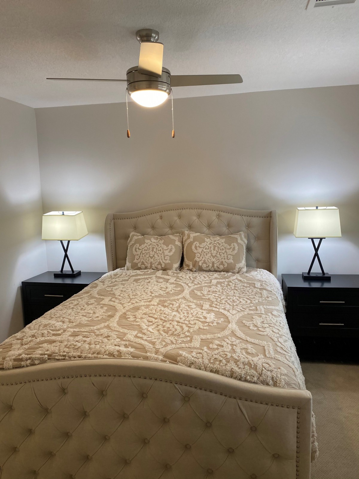 A cozy bedroom featuring a bed with patterned bedding, flanked by nightstands with matching lamps and a ceiling fan above.