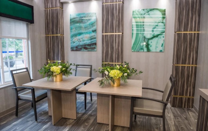 A modern meeting room with abstract artwork, two tables adorned with fresh flowers, and comfortable chairs.