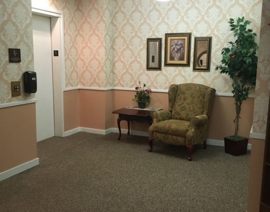 A quiet waiting area with an elevator, featuring a comfortable chair, side table, and decorative elements.