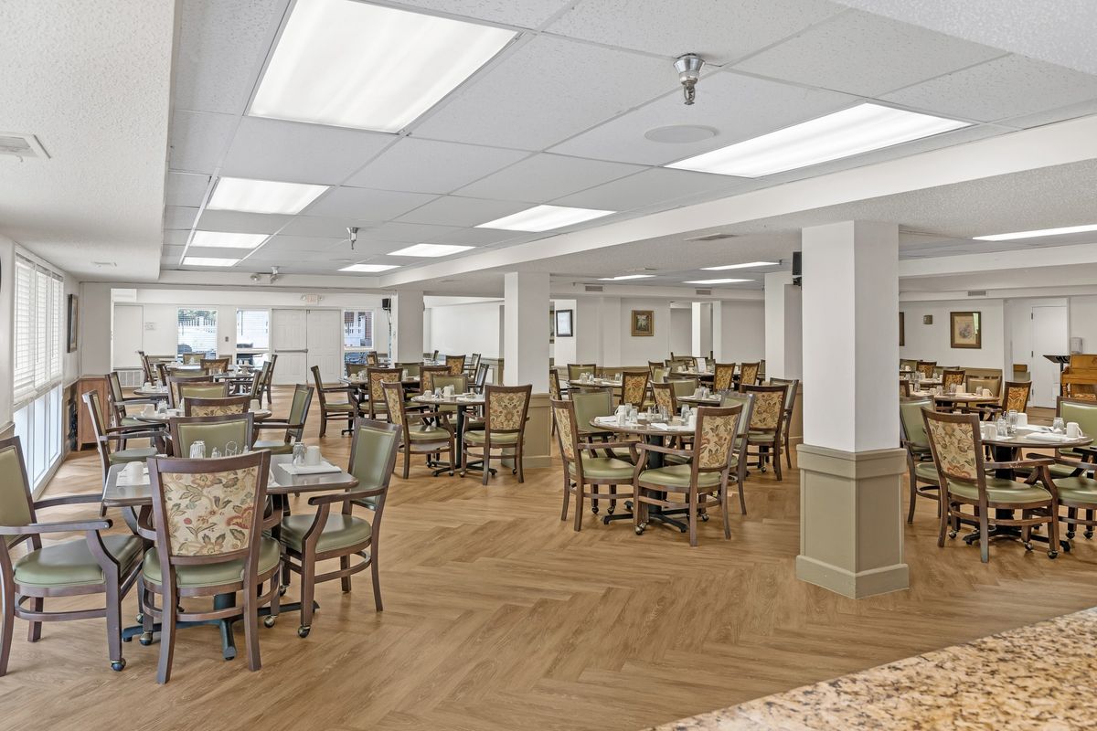 An empty dining room with neatly arranged tables and chairs, featuring a wooden floor and overhead lighting.