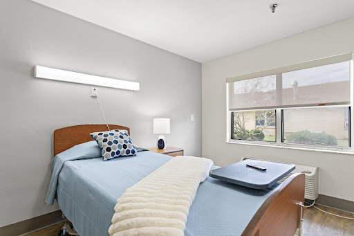 A serene and well-lit bedroom featuring a neatly made bed with blue bedding, decorative pillows, and a bedside table.