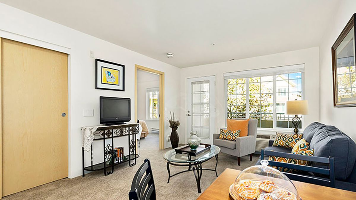 A cozy living room with modern furniture, featuring a TV and large windows that let in natural light.