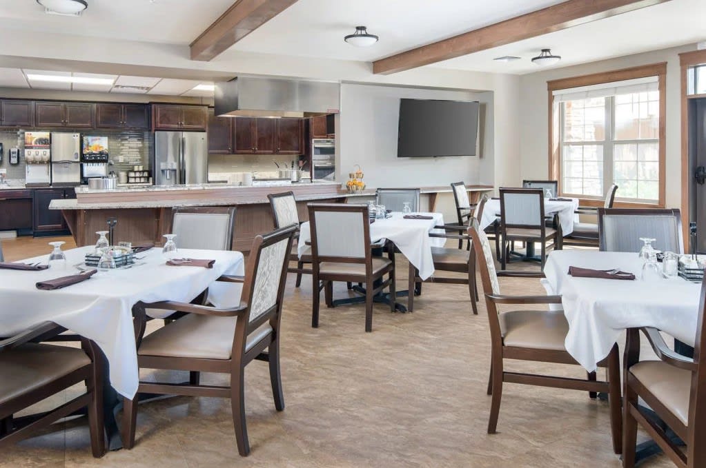 A modern dining area with neatly arranged tables and chairs featuring white tablecloths.