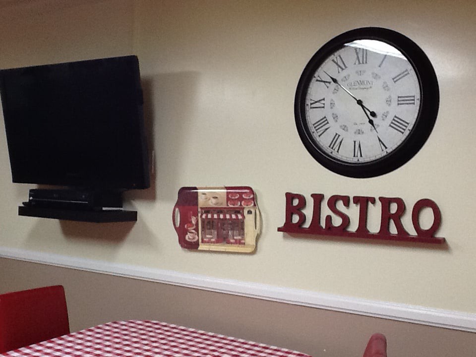 A cozy bistro-themed room with a large clock, TV, and red and white decor.