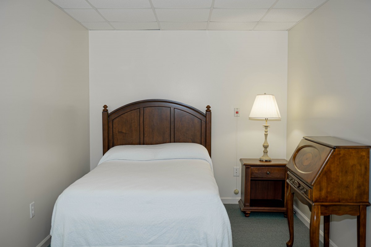A simple bedroom with a single bed and a nightstand with a lamp.
