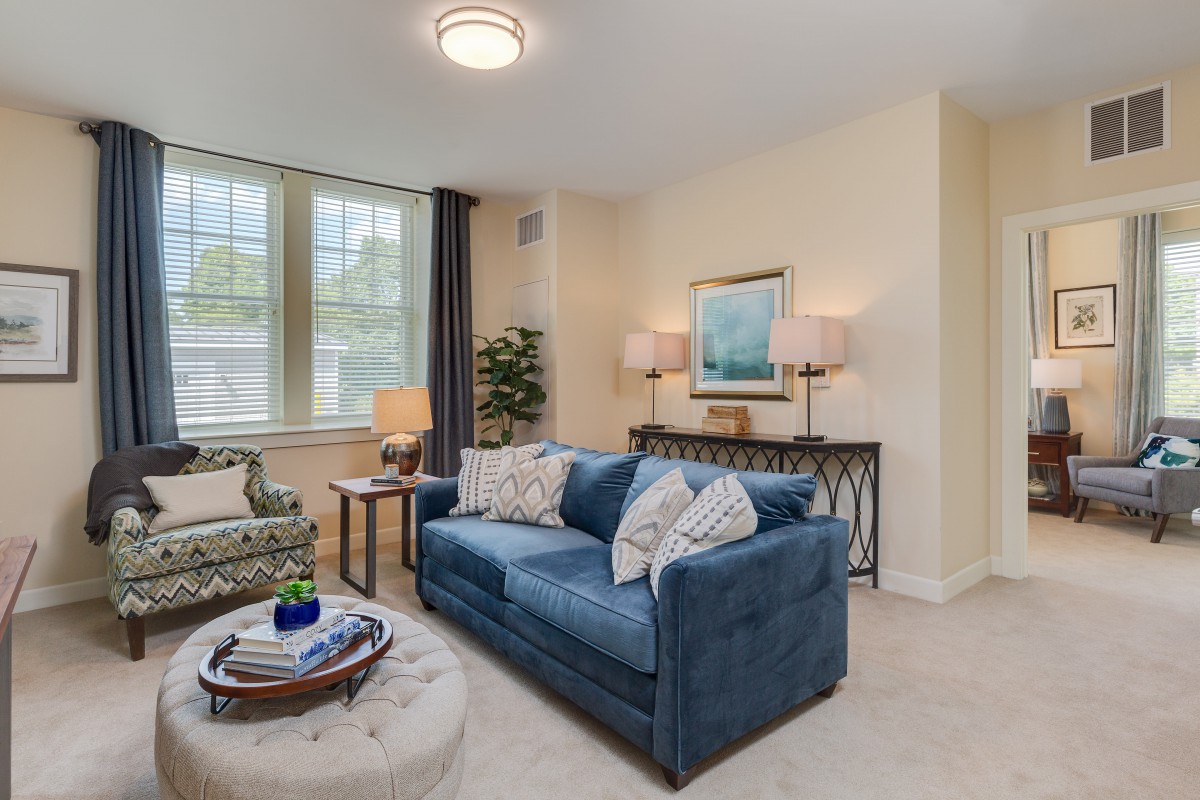 A cozy and well-decorated living room featuring a blue sofa, elegant lamps, and large windows.