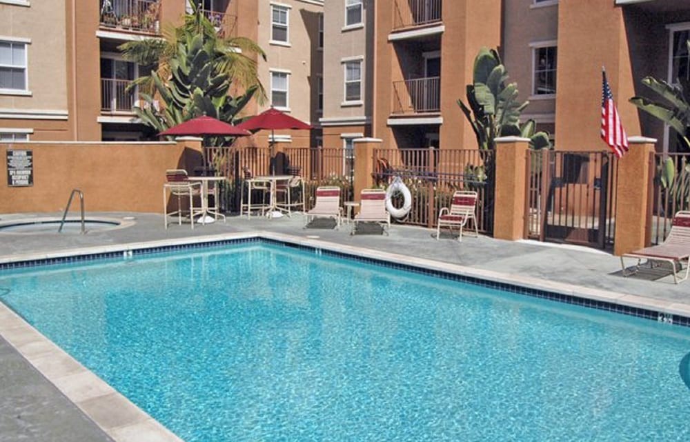 Outdoor swimming pool area with sun loungers and umbrellas at an apartment complex.