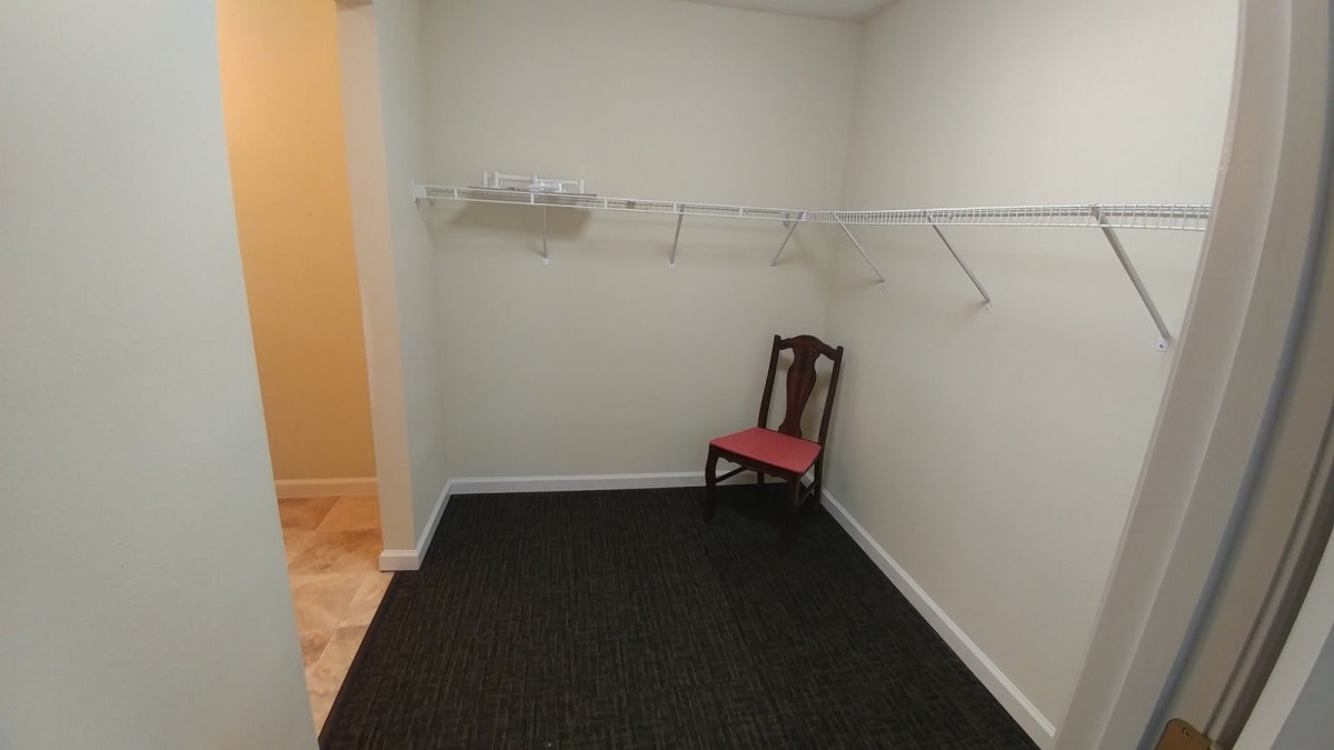 An empty walk-in closet with a single chair and hanger rods.
