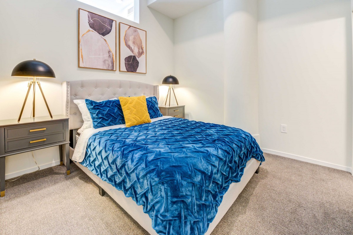 A cozy bedroom with a modern design, featuring blue bedding, decorative pillows, and wall art.
