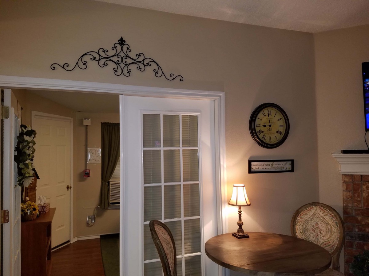 A cozy dining corner featuring a round table with chairs, decorative wall elements, a clock, and French doors.