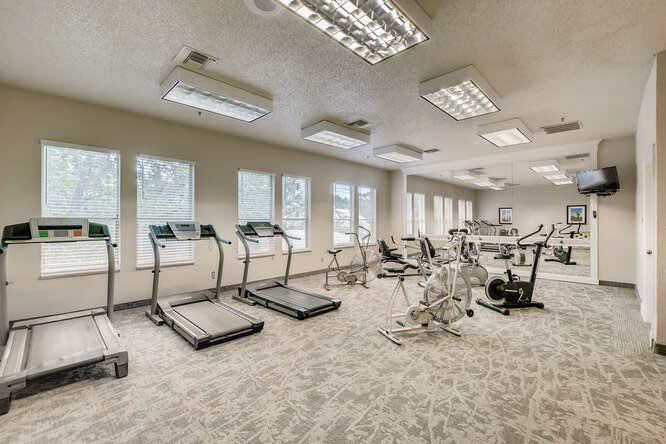 A well-lit gym with various exercise equipment including treadmills and stationary bikes.