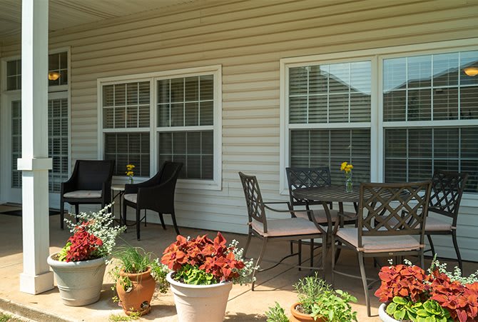 A cozy patio area with chairs, a table, and potted plants in front of two large windows.