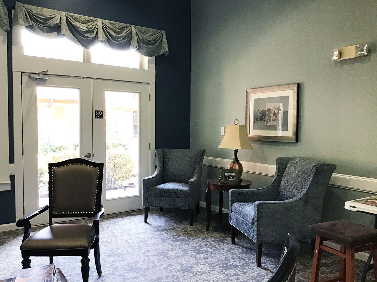 A cozy living room with elegant decor, featuring upholstered chairs and a side table with a lamp near a large window.
