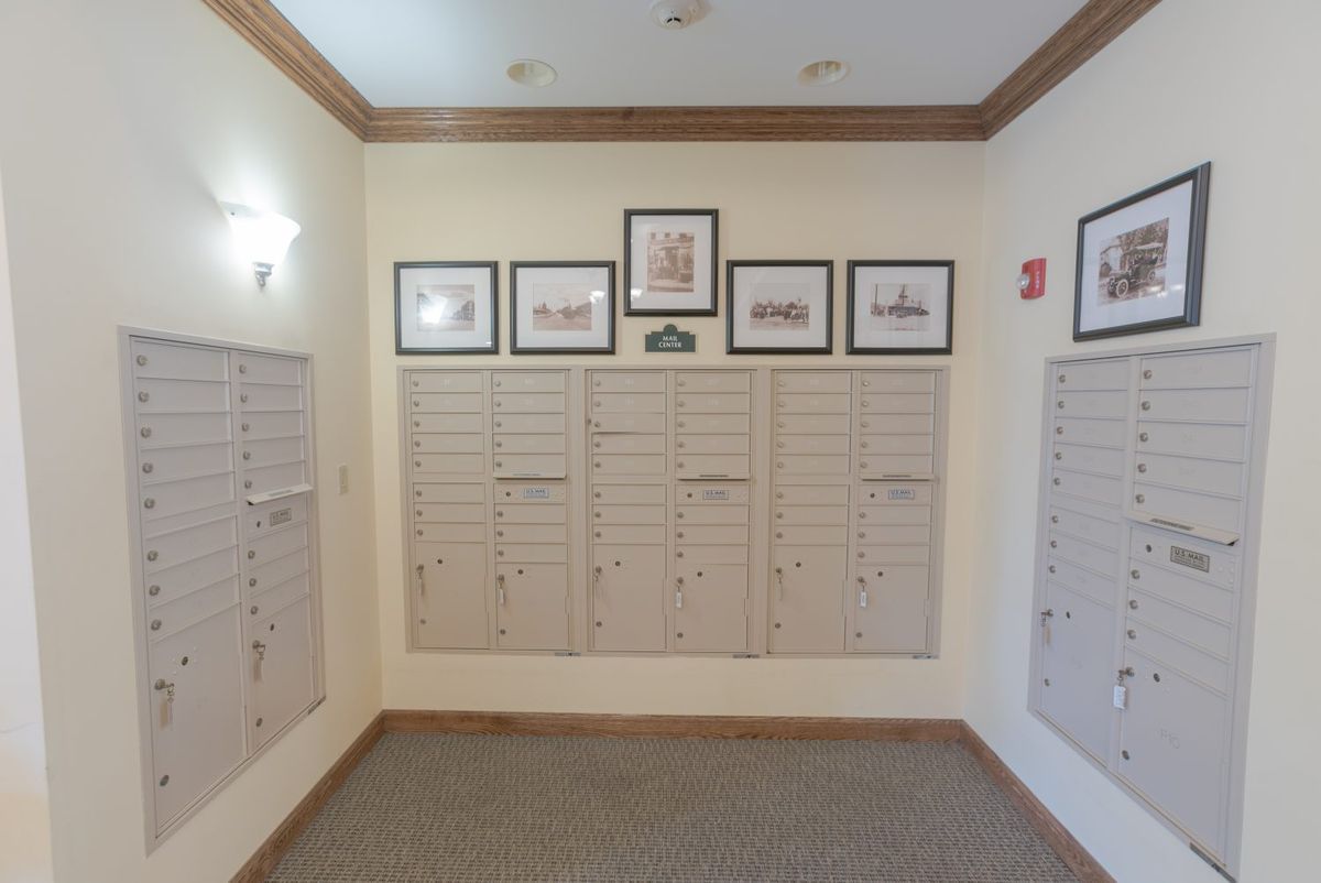 An indoor apartment hallway featuring multiple wall-mounted mailboxes and framed artwork above them.