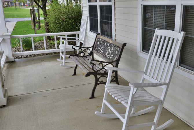 A cozy porch with a bench and white rocking chairs.