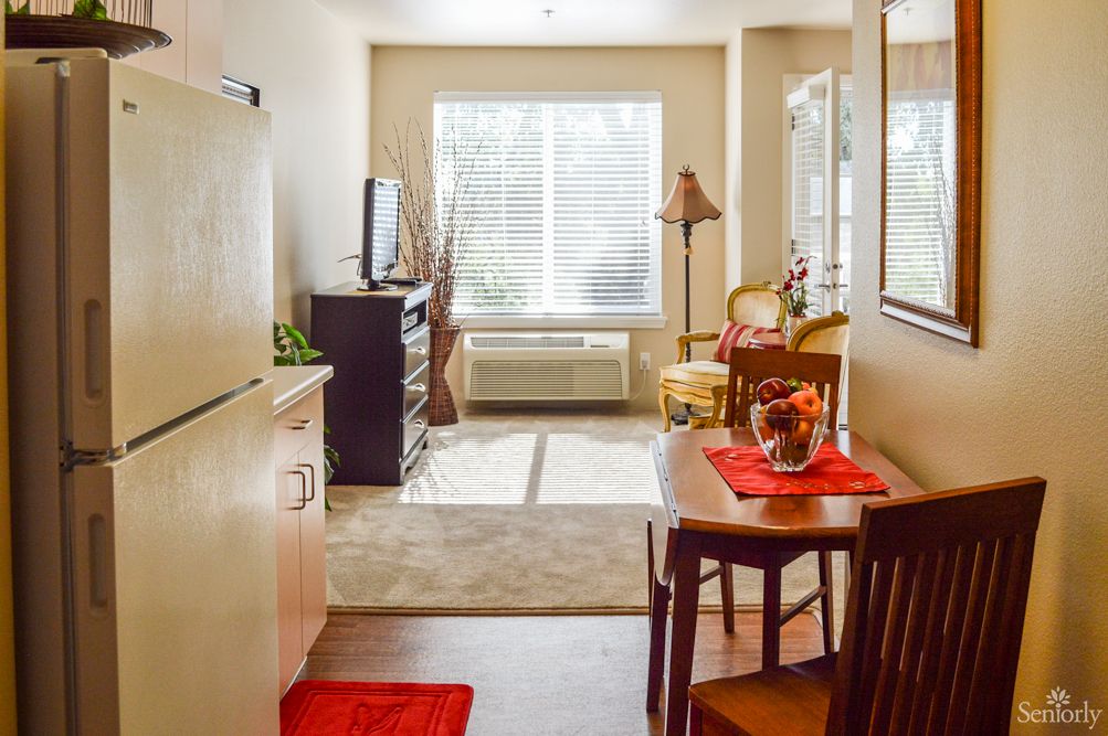 A cozy kitchen and dining area with a small table and chairs, illuminated by sunlight streaming through the window.