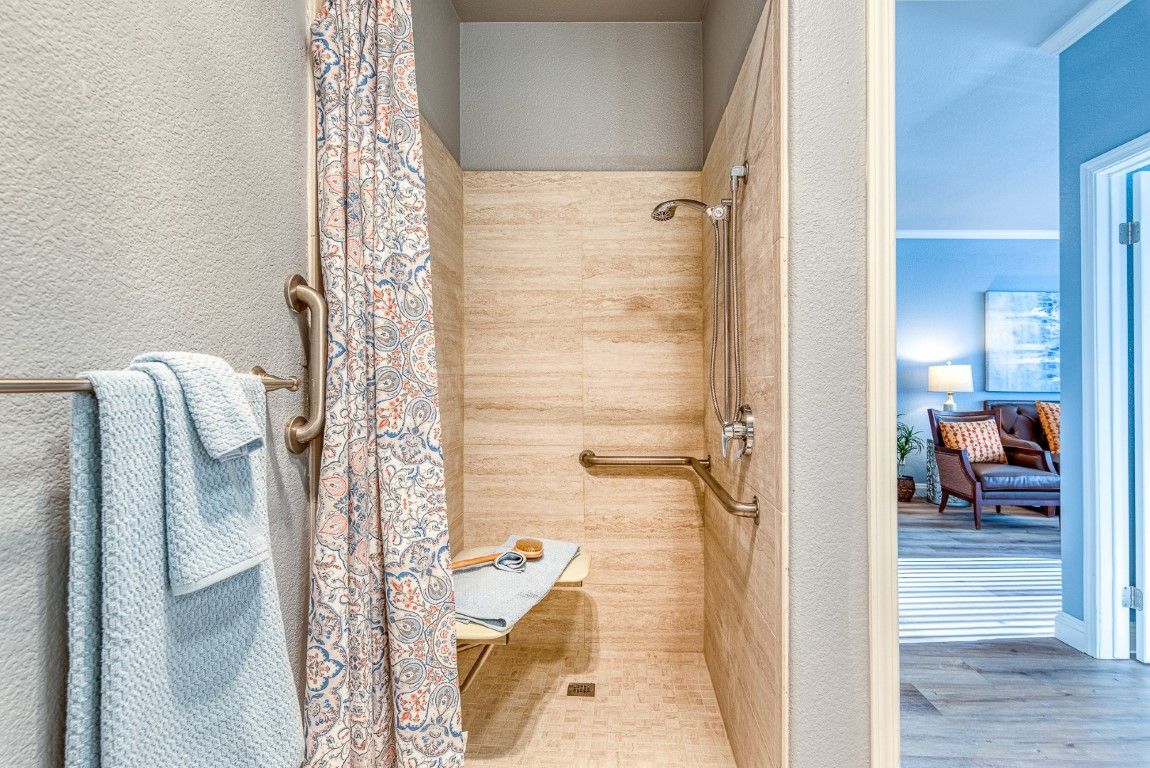A modern, accessible shower with handrails and a bench, featuring a patterned shower curtain.