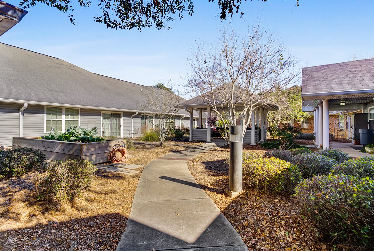 A scenic view of a landscaped pathway leading to a building surrounded by trees and bushes on a clear day.