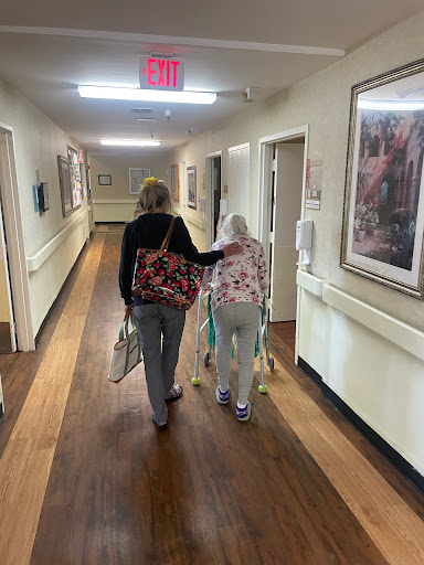 A caregiver gently assists an elderly woman as they walk down a corridor.