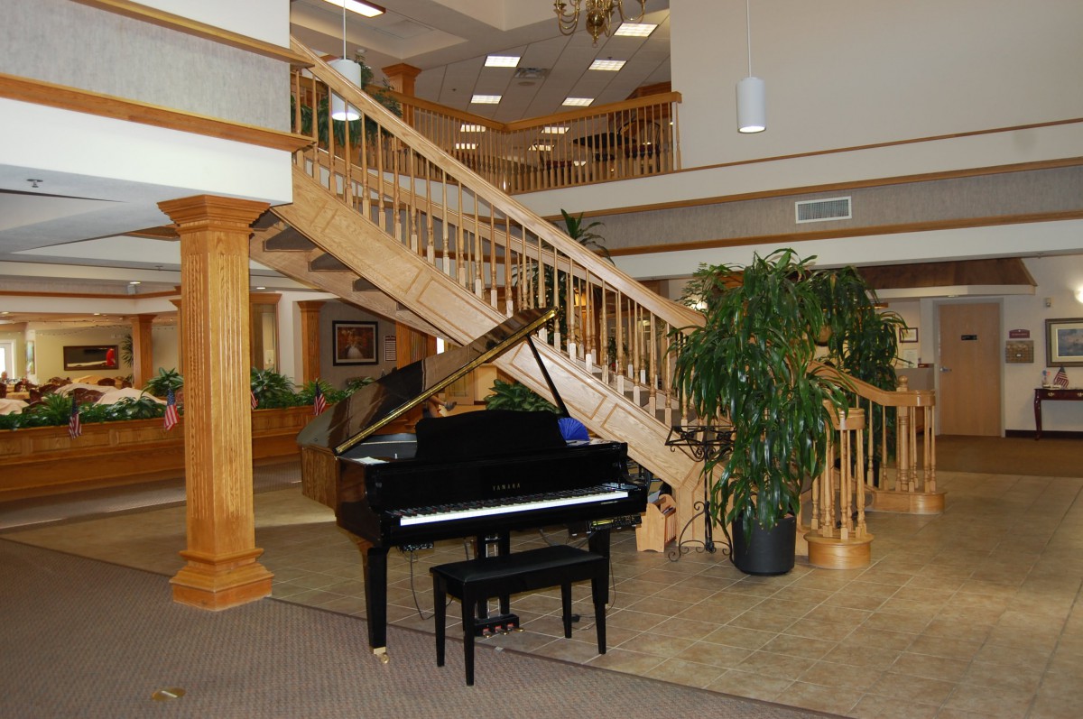 A grand piano in a spacious lobby with a wooden staircase and indoor plants.