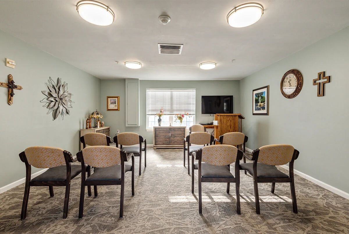 A small conference room with neatly arranged chairs facing a television, featuring soft lighting and tasteful decorations.