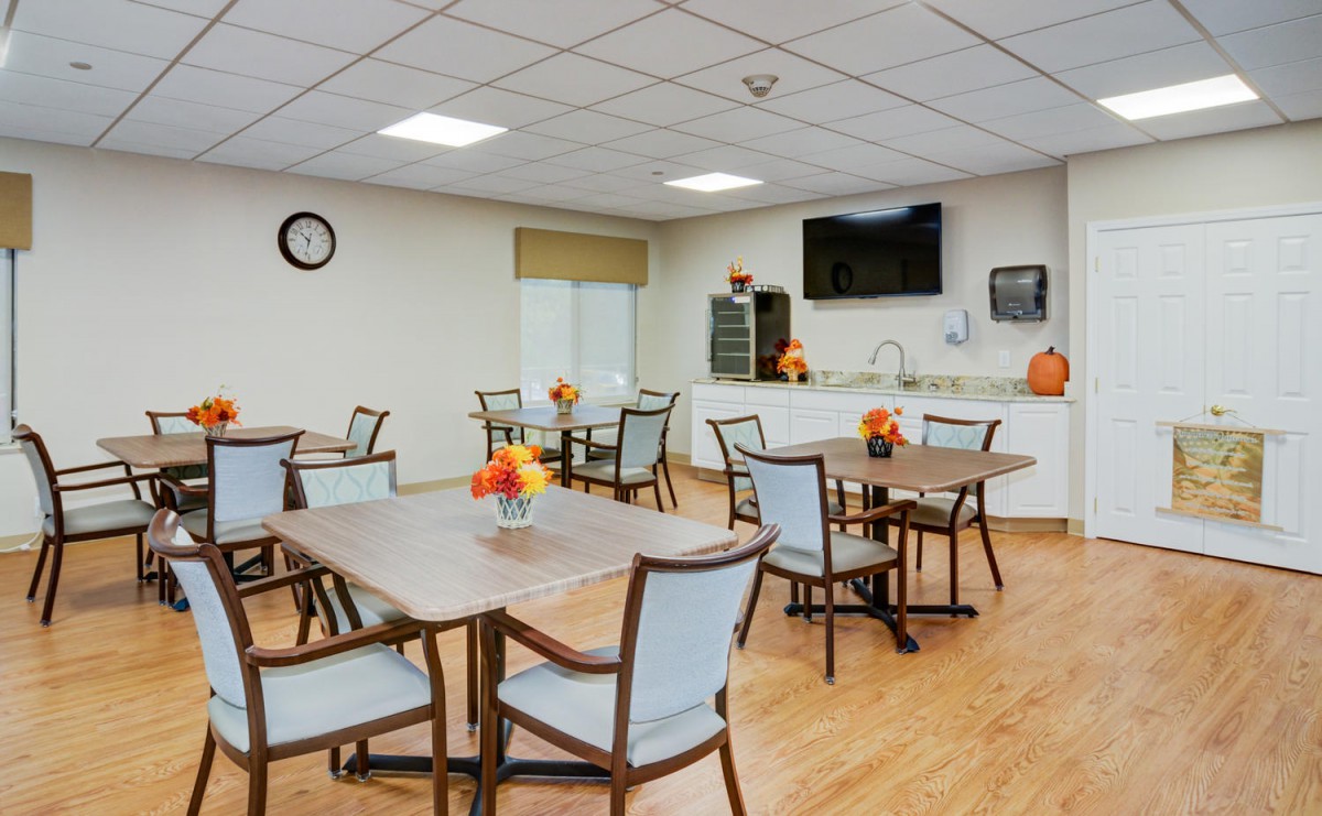 A modern dining area with neatly arranged tables and chairs, featuring a television on the wall.