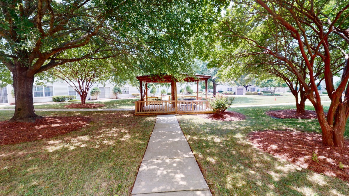 A peaceful garden with a pathway leading to a gazebo surrounded by lush trees.