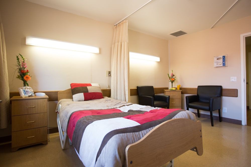 A well-furnished hospital room featuring a bed, chairs, and curtain for privacy.