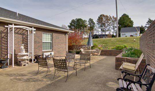 A cozy outdoor patio with metal chairs and a garden umbrella beside a brick house.