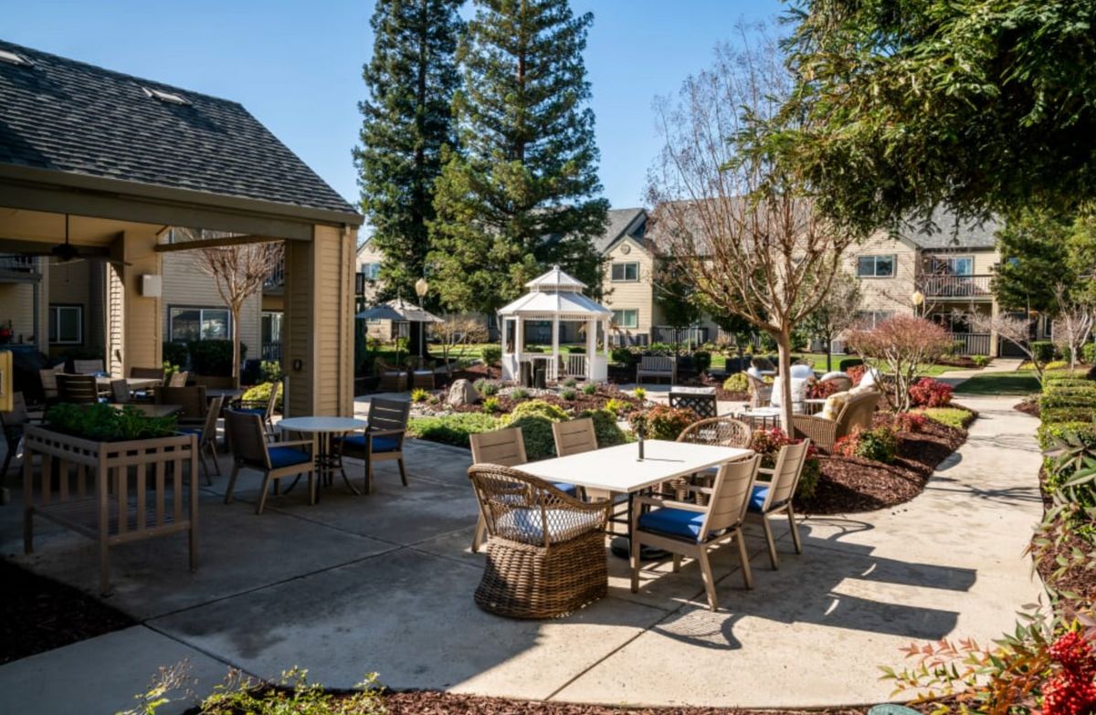 A sunny outdoor patio area with tables, chairs, a gazebo, and surrounding garden.