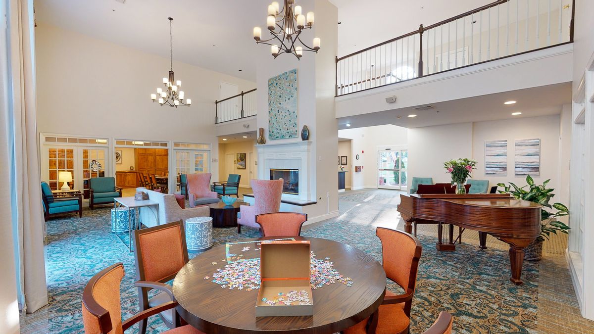 A spacious and elegantly furnished living area featuring a table with chairs, a prominent chandelier, and a cozy fireplace.