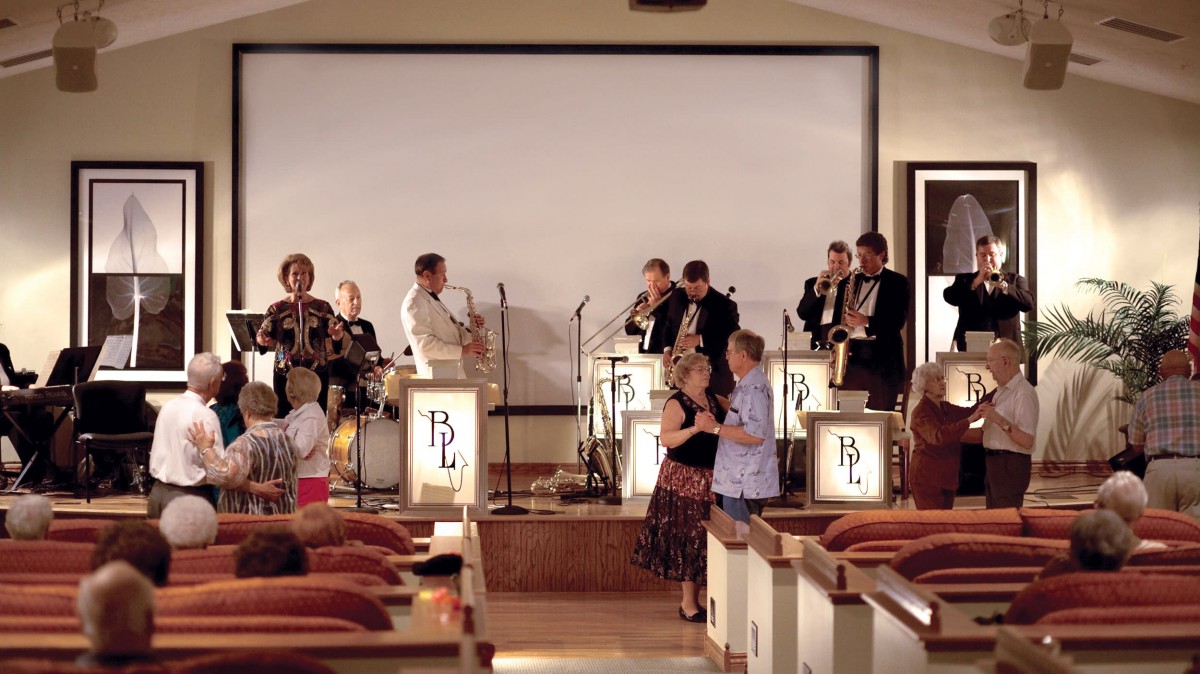 A band performs on stage while people dance in front of them at an event.