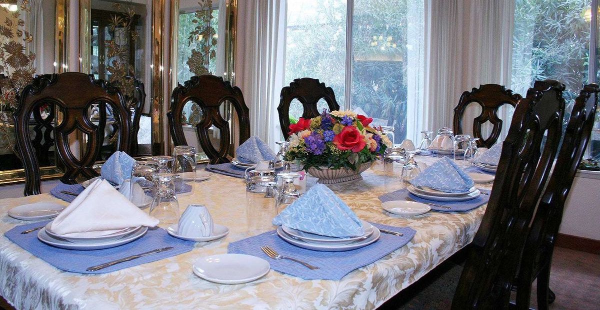 A formal dining table elegantly set with blue napkins, silver cutlery, and a vibrant floral centerpiece.