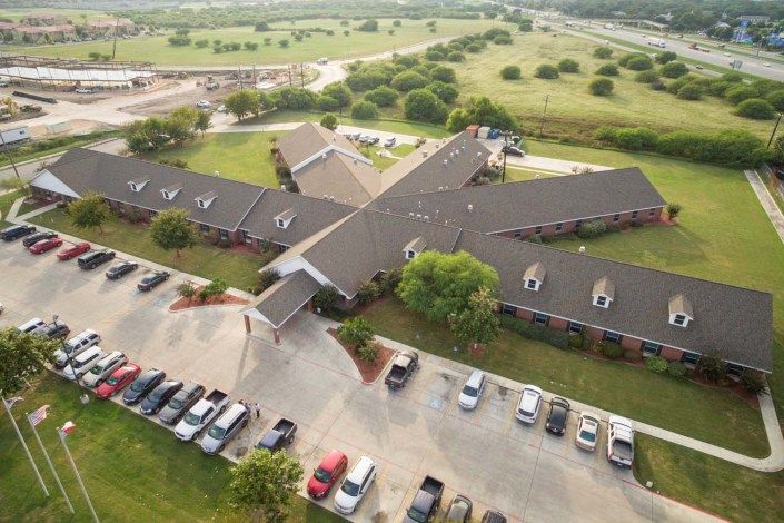 Aerial view of a building with a surrounding parking lot in a rural landscape.