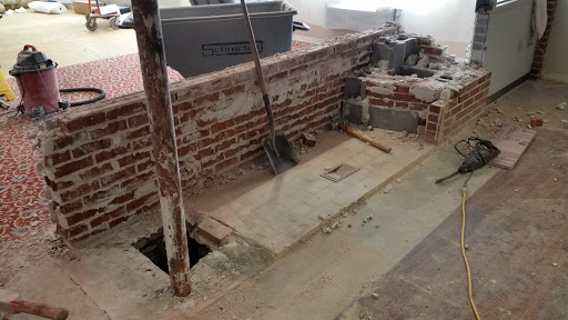 A construction site showing unfinished flooring and tools, with a brick wall as the backdrop.