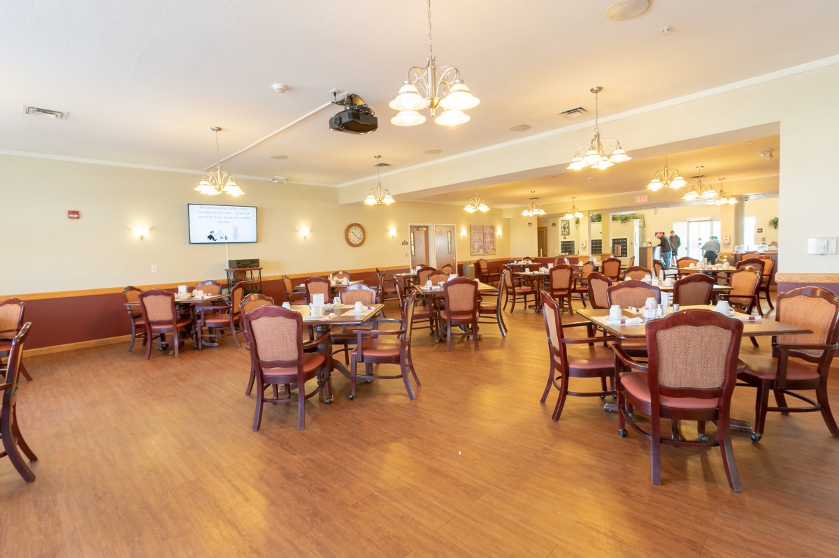 An inviting dining room with neatly arranged tables and chairs, warmly lit by elegant lighting fixtures.