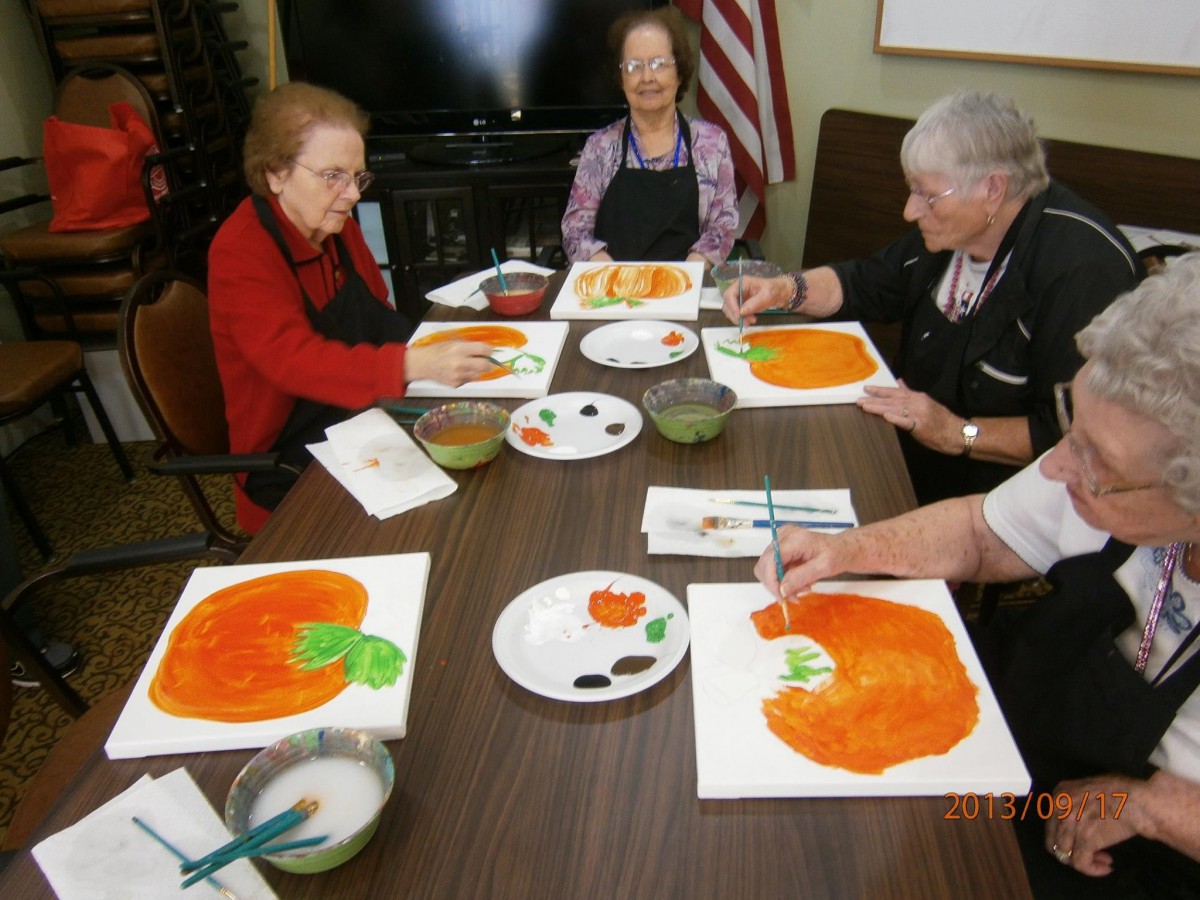 A group of seniors enjoying a painting class, creating pumpkin-themed artwork together.