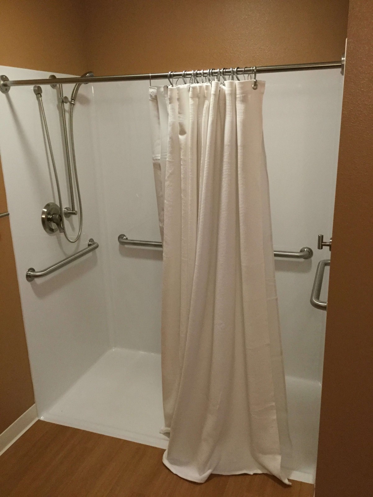 An accessible shower with grab bars and a handheld showerhead.