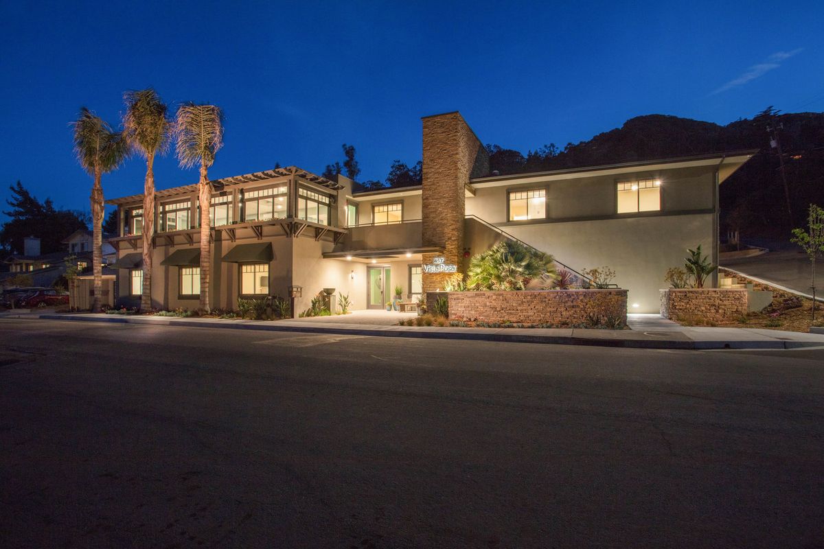 A modern house illuminated at night with palm trees in the foreground.